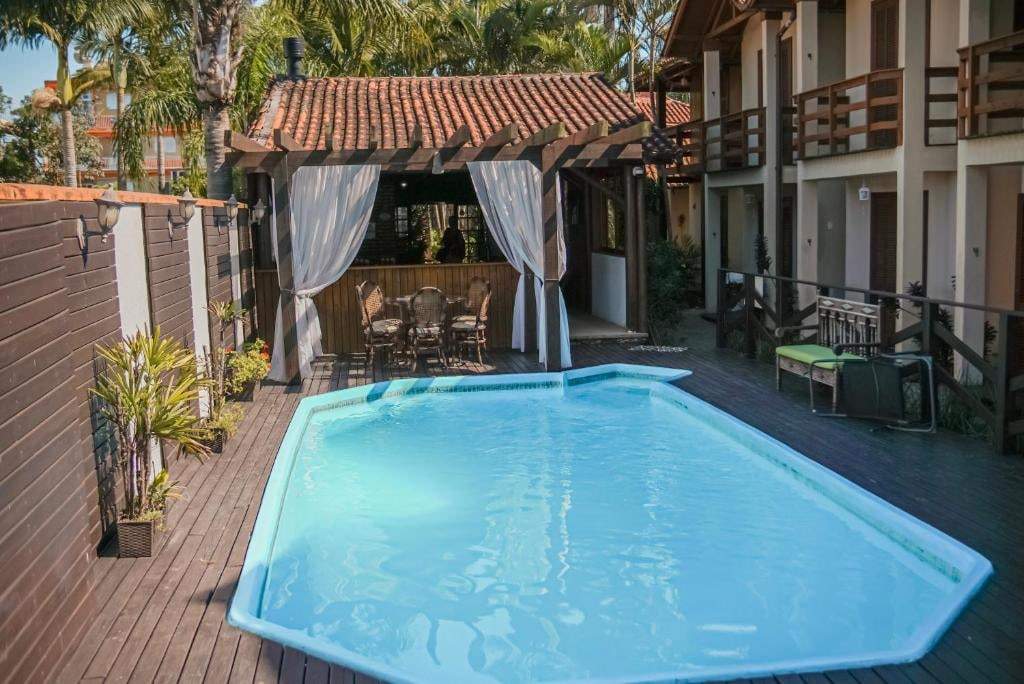 Piscina com deck de madeira e pergolado ao lado das suítes